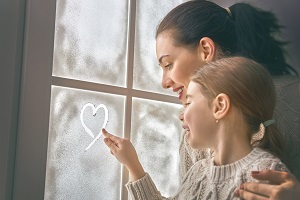 Mom and daughter looking out window at snow